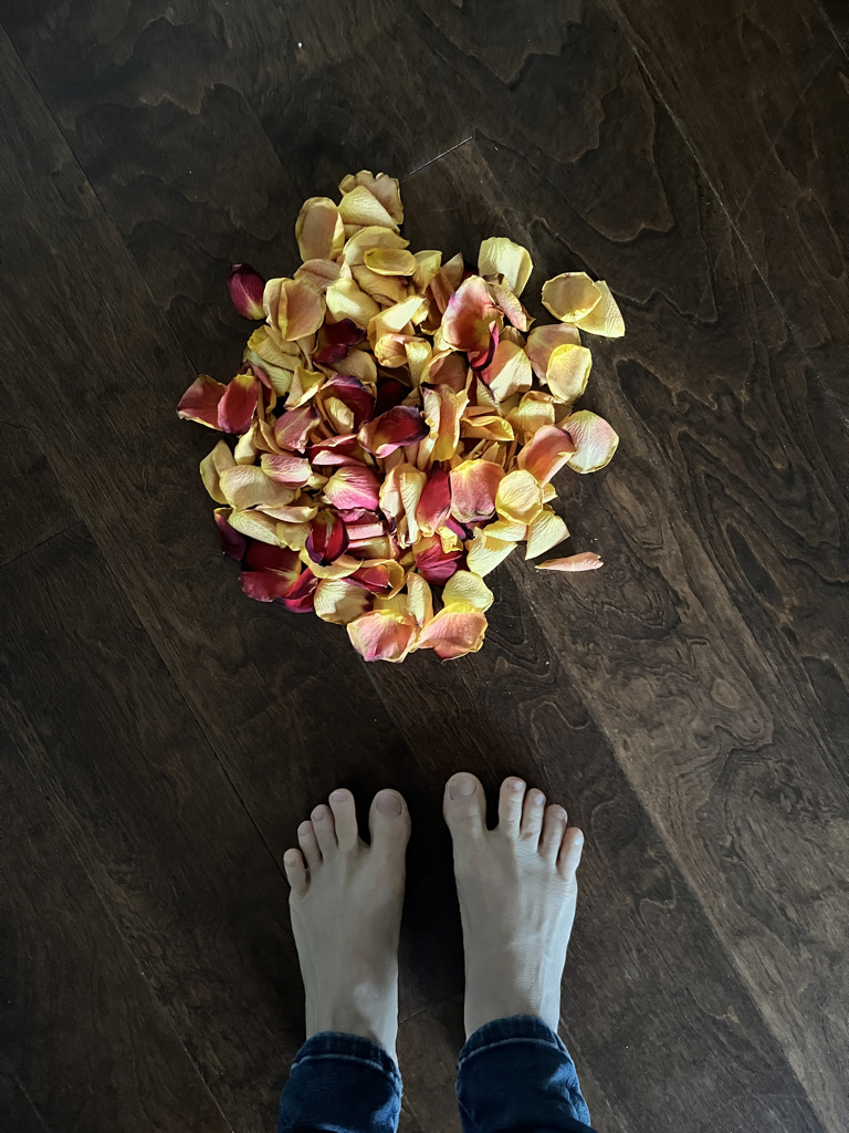 Bare feet resting on a wood floor beside a pile of rose petals